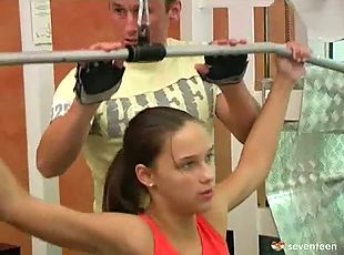 A teenage girl is working out at a gym. A guy is standing behind her....